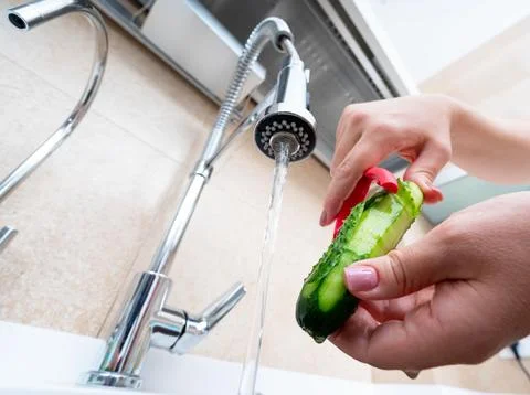 Preparing a fresh cucumber by peeling it under running water in the kitchen sink Stock-Fotos