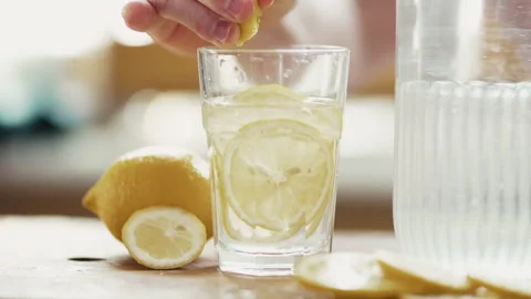 Preparing Fresh Lemon Water: Man's Hand Dropping Fruit and Pouring Mineral Water Stock Footage 332680608