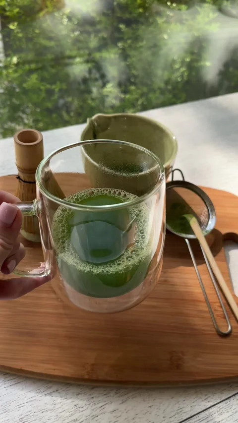 Preparing fresh matcha tea ritual by a sunlit window with whisk Stock Footage 320851415