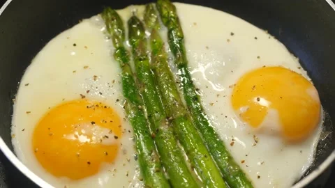 Preparing fried eggs with fresh asparagus on frying pan Stock Footage 146868350
