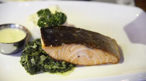 Preparing grilled salmon steak served with stirred spinach Stock Footage 63303223