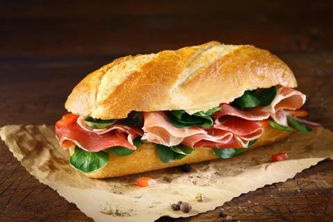Preparing a ham and basil baguette Stock Photos