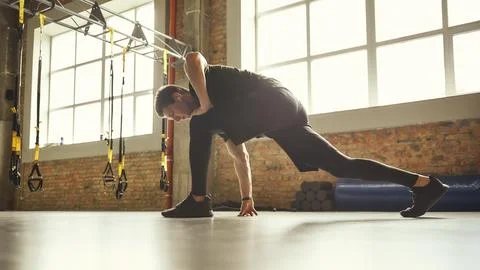 Preparing his muscles. Side view of young sporty man in sportswear stretching Stock Photos