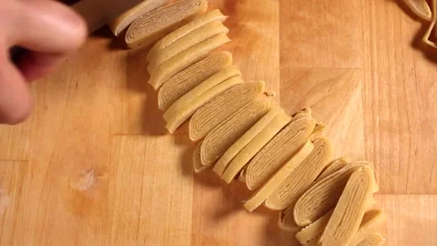 Preparing homemade egg pasta. The woman's hands cut pasta dough with a knife Stock Footage 219582874