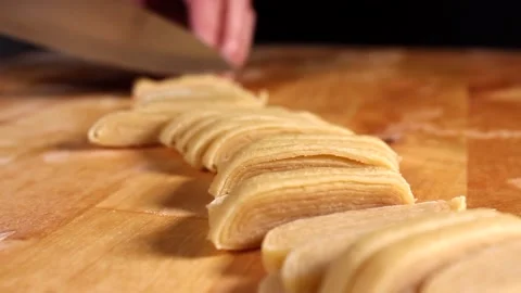Preparing homemade egg pasta. The woman's hands cut pasta dough with a knife Stock Footage 219582912