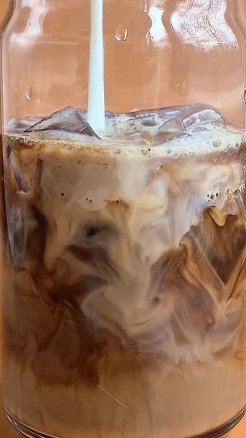 Preparing iced coffee with milk and ice in a glass cup Video stock 304667068