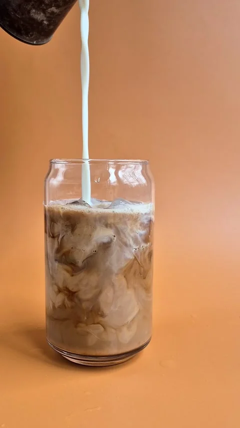 Preparing iced coffee with milk and ice in a glass cup Stock Footage 304667096