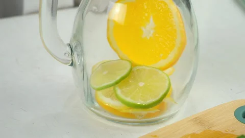 Preparing lemonade putting citrus slices into glass jug on kitchen at home. Video stock 313116586