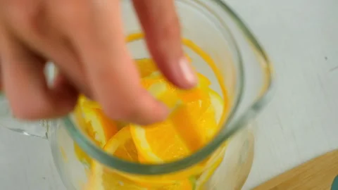 Preparing lemonade putting citrus slices into glass jug on kitchen top view. Stock Footage 313116798