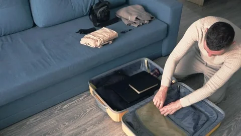 Preparing luggage for vacation. The man puts his phone and some clothes on t Stock Footage 275679612