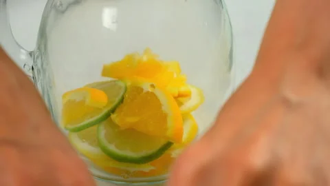 Preparing making lemonade putting citrus slices into glass jug on kitchen. Stock Footage 313116661
