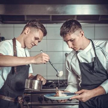Preparing meat with sauce by two young chefs Stock-Fotos