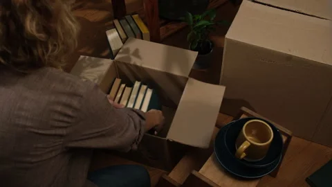 Preparing for move, removal concept. Woman packs books into moving boxes at home Stock Footage 257549375