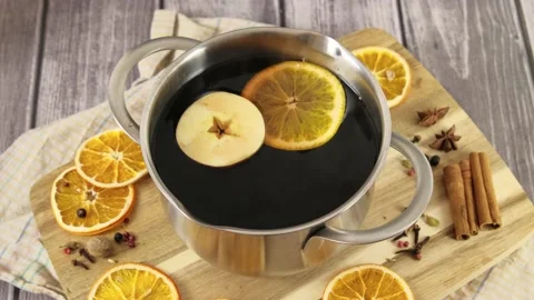 Preparing mulled wine, woman's hand putting orange slices into pan with red wine Stock Footage 227028136