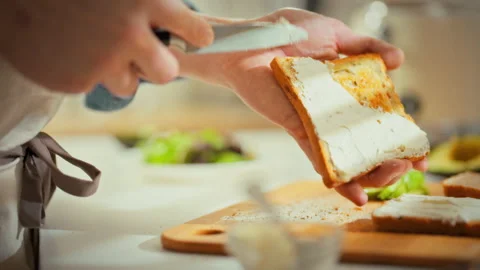 Preparing a nutritious breakfast a man in his home kitchen toasts bread spre Stock Footage 335462611