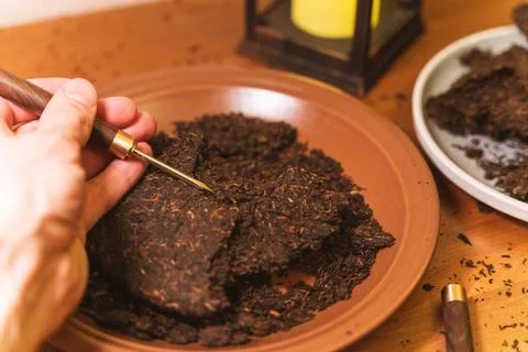 Preparing pu-erh tea: hands using a tea knife to break up pressed tea leaves Foto stock