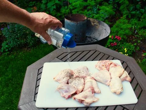 Preparing raw chicken thighs for bbq with salt, pepper and herbs with a sha.. Stock Photos