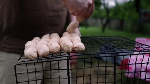 Preparing Raw Sausages for Grilling on a Barbecue Rack Outdoors Stock Footage 337105197