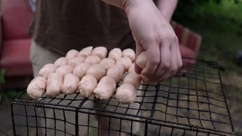 Preparing raw sausages for grilling on a barbecue rack outdoors Stock Footage 337105240