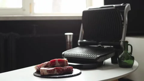 Preparing raw steaks for grilling on an electric grill in a kitchen Stockbeeldmateriaal 342280635