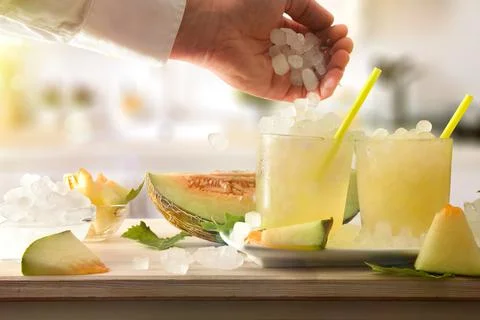 Preparing refreshing melon drink by throwing cubes into a glass Stock Photos