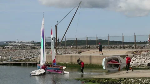 Preparing to sail sailing dinghies two people walking into water Stock Footage 51255630