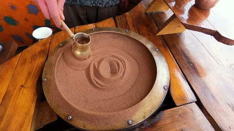 Preparing Turkish coffee in a copper cezve on hot sand is an old Turkish way of Stock Footage 177605003