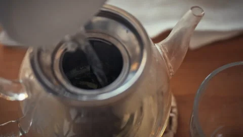 Preparing a warm beverage with a silver teapot and glass Stock Footage 323876723