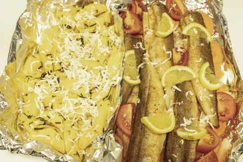 Prerape raw spiced hake and potate for a bake in the oven with lemon, tomat.. Stock Photos