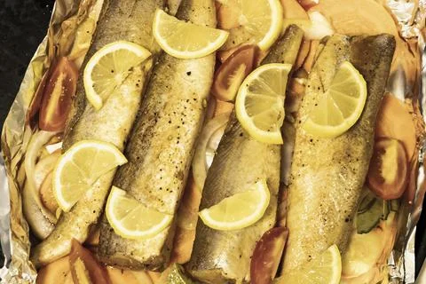 Prerape raw spiced hake for a bake in the oven with lemon, tomatoes, carrot.. Stock Photos