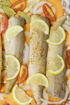Prerape raw spiced hake for a bake in the oven with lemon, tomatoes, carrot.. Stock Photos