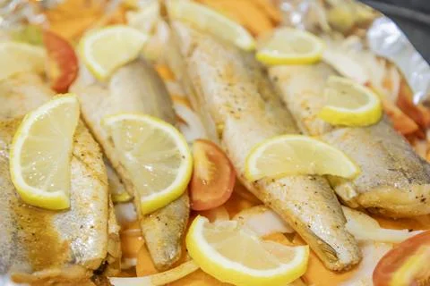 Prerape raw spiced hake for a bake in the oven with lemon, tomatoes, carrot.. Stock Photos