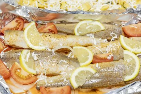Prerape raw spiced hake for a bake in the oven with lemon, tomatoes, carrot.. Stock Photos