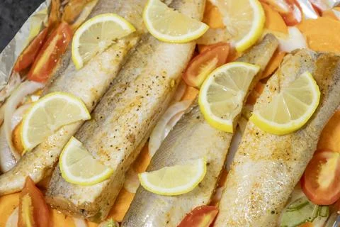 Prerape raw spiced hake for a bake in the oven with lemon, tomatoes, carrot.. Stock Photos