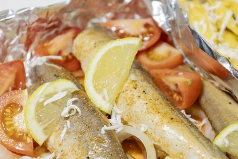 Prerape raw spiced hake for a bake in the oven with lemon, tomatoes, carrot.. Stock Photos