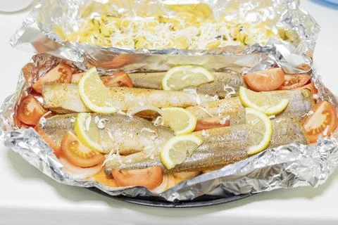 Prerape raw spiced hake for a bake in the oven with lemon, tomatoes, carrot.. Stock Photos