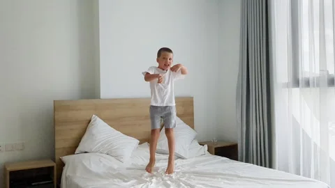 Preschool boy jumping on bed. White cozy home interior. Stock Footage 255815891