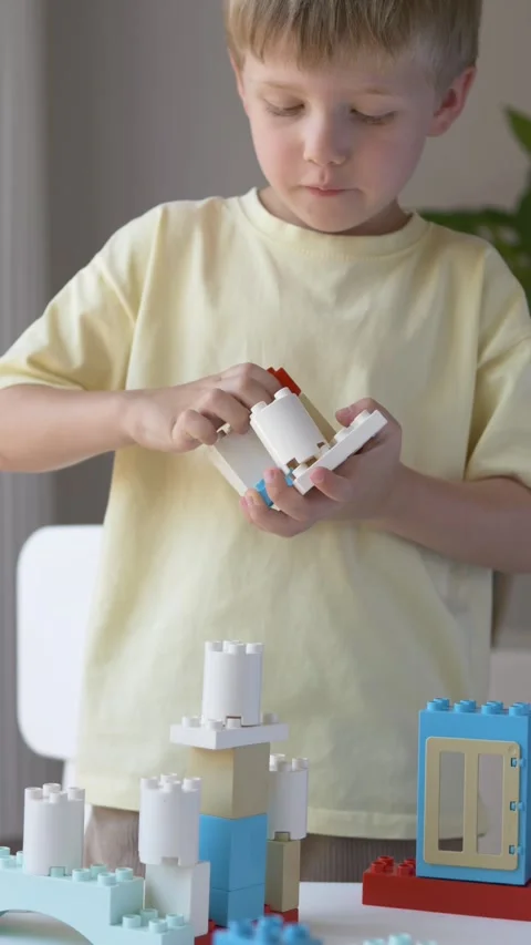 Preschool boy studies a construction block piece before adding it to his Stock Footage 345653694