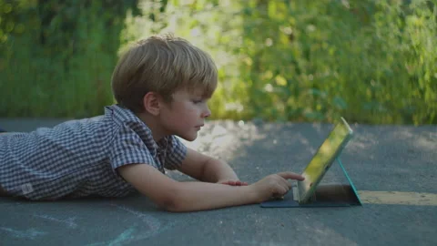 Preschool boy using tablet computer laying on the ground in park. Kid watching Video stock 138173660