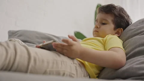 Preschool kid lying on sofa looking at mobile screen Stock Footage 245590323
