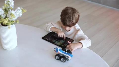 A preschool kid uses tablet pc, controls the robot made of bricks Stock Footage 253975393