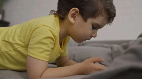 Preschool smiling kid lying on sofa looking at mobile screen Stock Footage 245594309