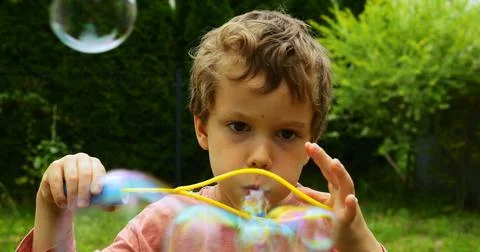 Preschooler boy squeezes plastic frame increasing size of bubbles blowing Stock Photos