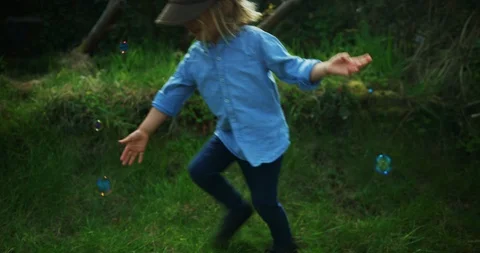 Preschooler boy wearing a hat chasing bubble sin garden Stock Footage 130122218