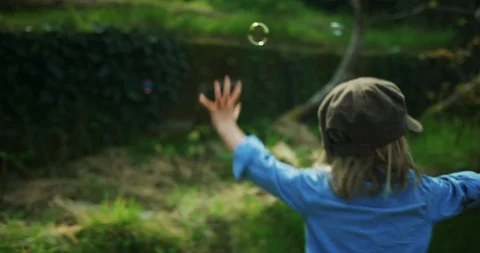 Preschooler with hat seeing bubbles in garden and chasing them Stock Footage 130121430