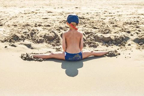 Preschooler makes leg-split on soft sand of seashore Stock Photos