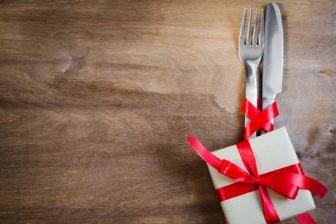 Present and Silverware Decorated with Red Ribbon on Wooden Background. Stock Photos