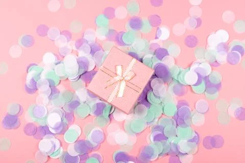 Present box on pink background with multicolored confetti. Stock Photos