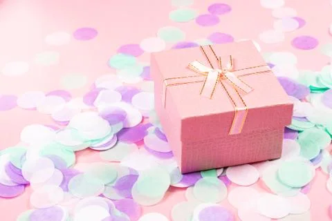 Present box on pink background with multicolored confetti. Stock Photos