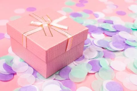 Present box on pink background with multicolored confetti. Stock Photos